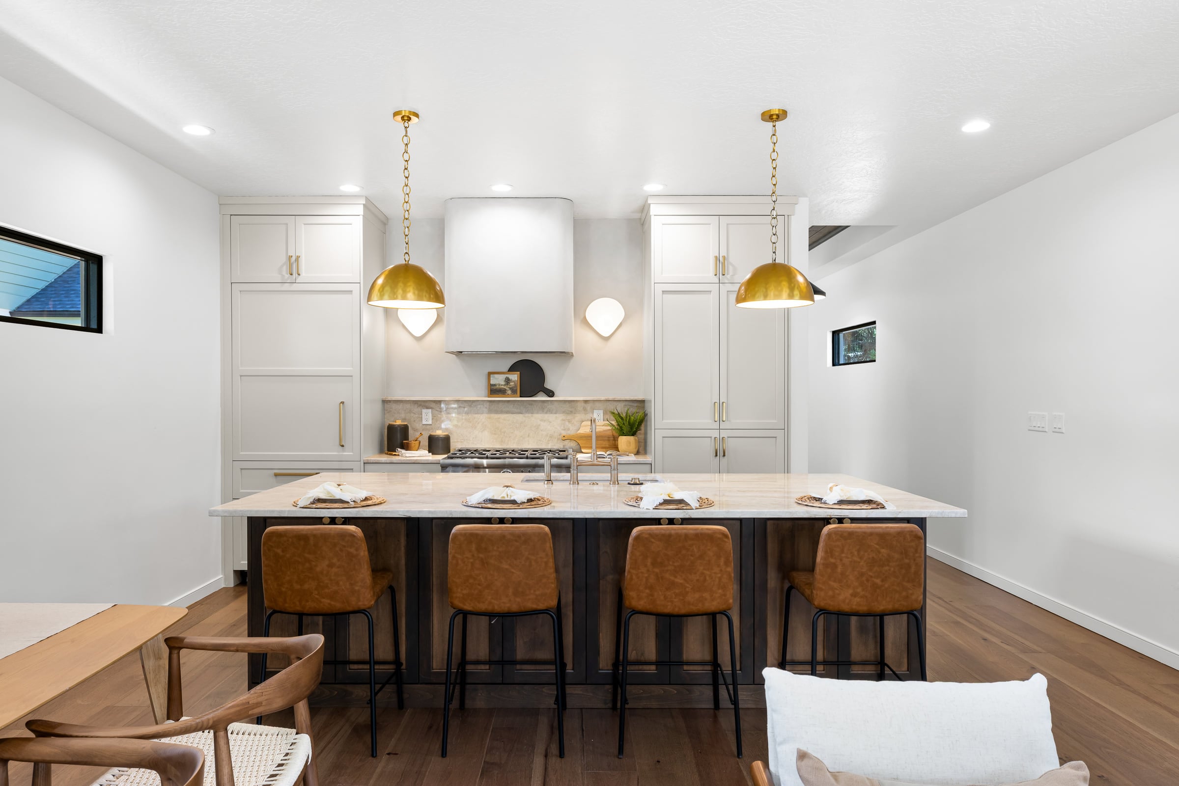 Kitchen of the 20th Street Residence: a stone-topped island with four leather stools, white cabinetry, brass dome pendants, and a plaster range hood.